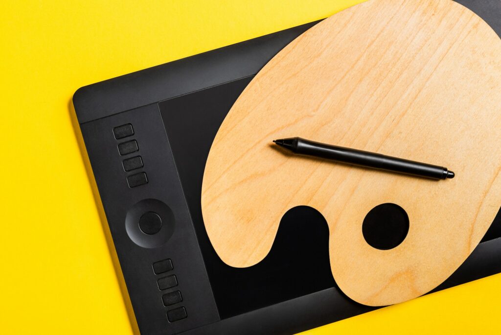 Top View of Wooden Palette And Graphics Tablet With Stylus on Yellow Surface